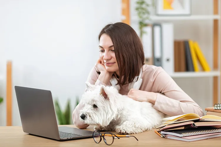 Mujer sonriendo con su perro frente a su portátil