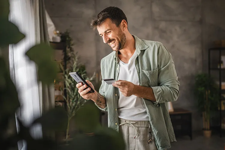 Hombre sonriendo con su celular y tarjeta en la mano