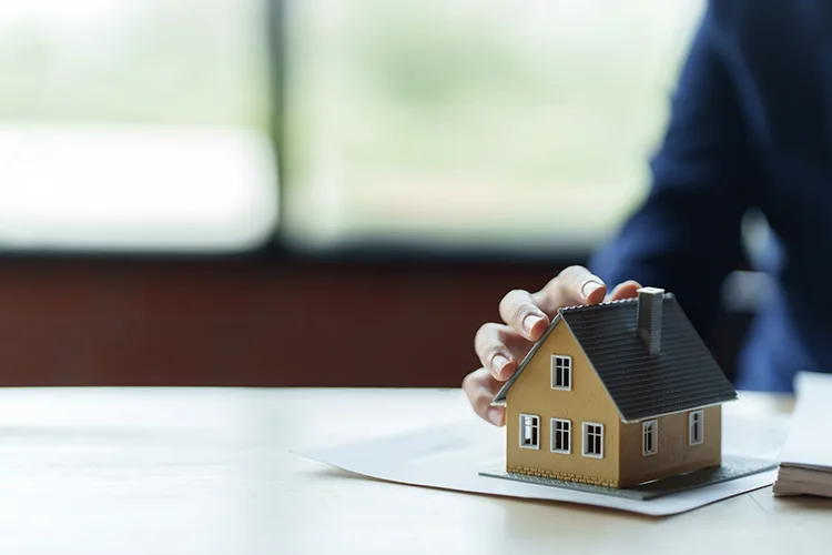 Mano tocando maqueta de casa para construcción en sitio propio