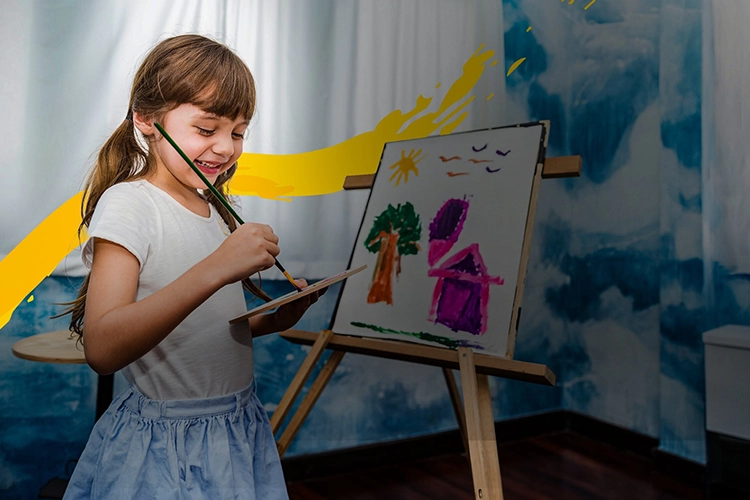 Niña con una paleta de pintura en sus manos frente a un caballete