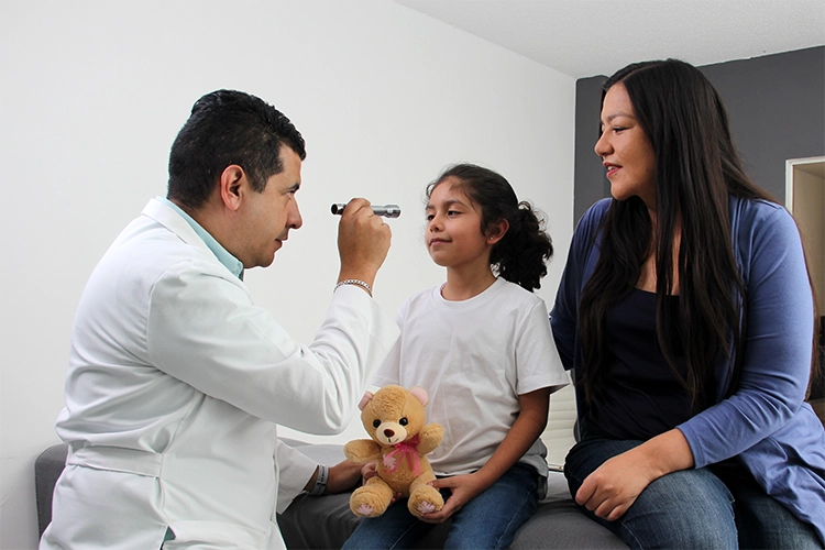 Médico revisando a una niña acompañada por su madre