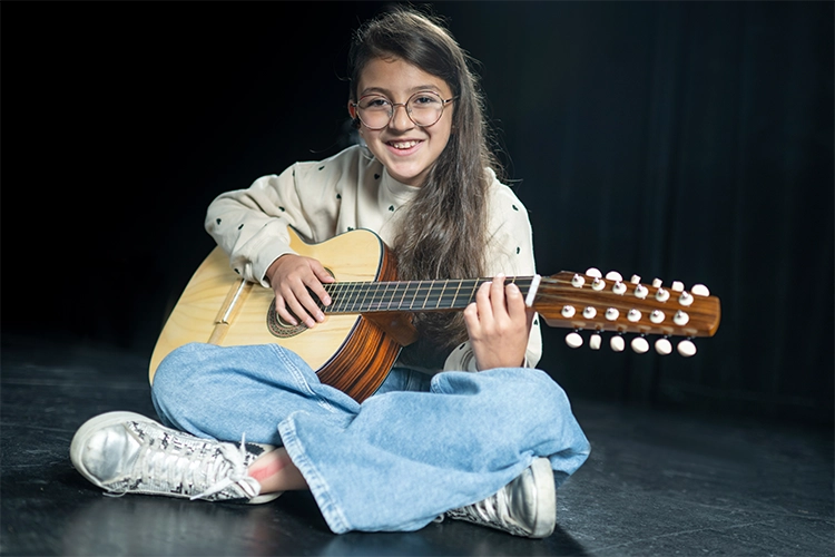 Una niña sentada sobre el suelo interpreta la guitarra.