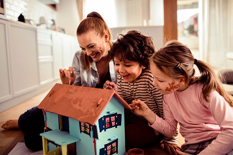 Madre e hijos sonriendo mientras diseñan una casa de juguete.