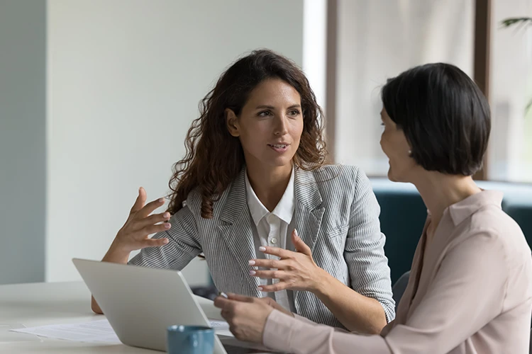 Dos mujeres conversando mientras revisan información en un portátil