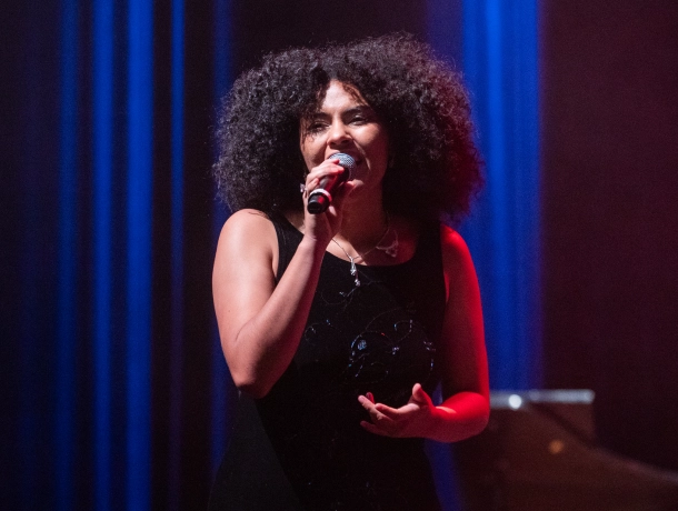 Cantante con micrófono durante una presentación en el Teatro Colsubsidio, bajo luces azules y rojas.