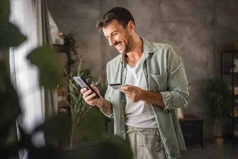 Hombre sonriendo con su celular y tarjeta en la mano
