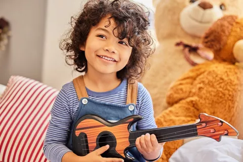 Un niño toca la guitarra mientras sonríe.