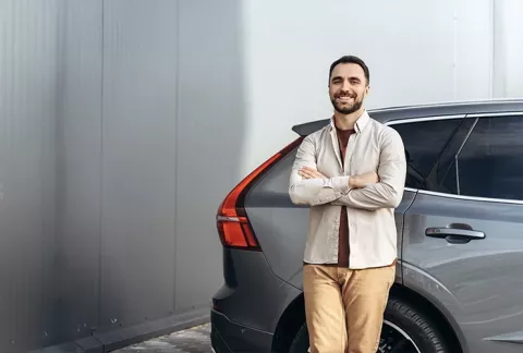 Hombre sonriente al lado de su auto asegurado con Colsubsidio.